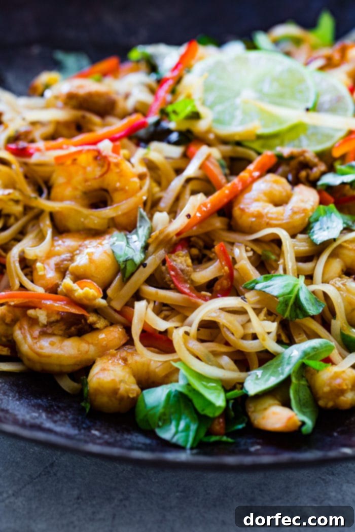 A vibrant plate of cooked shrimp, delicate rice noodles, vibrant red bell peppers, and fresh green basil leaves, garnished with bright slices of lime.