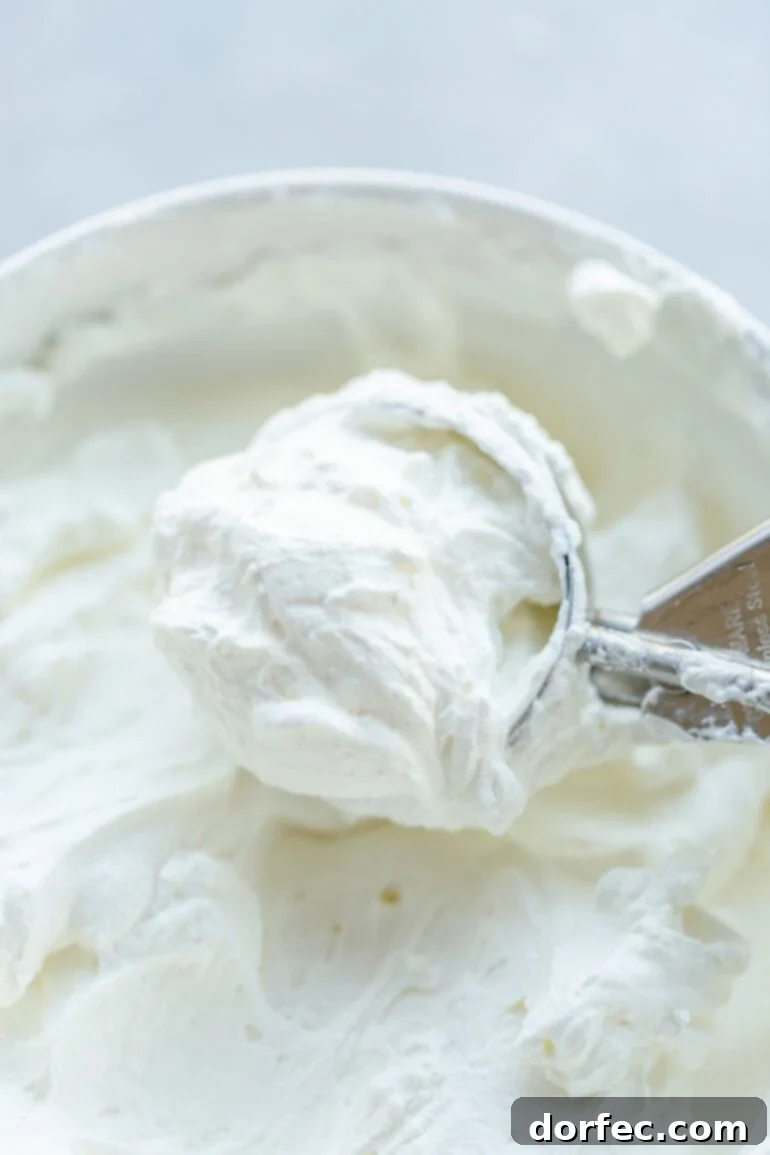 a photo of someone using an ice cream scoop to scoop up from mascarpone whipped cream from a big bowl of it