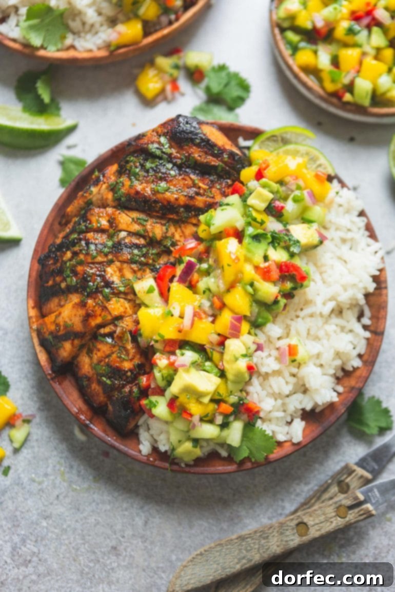 A vibrant dinner plate featuring perfectly grilled Mexican chicken, fluffy coconut rice, and a colorful, fresh mango salsa with chunks of fruit, peppers, onions, and cilantro.