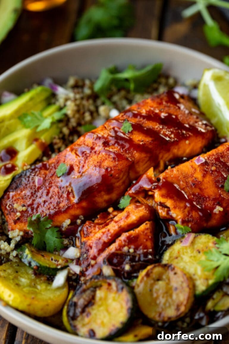 Two perfectly cooked salmon fillets glazed with a rich BBQ sauce, presented on a plate with vibrant grilled zucchini, fresh lime wedges, and creamy sliced avocado.