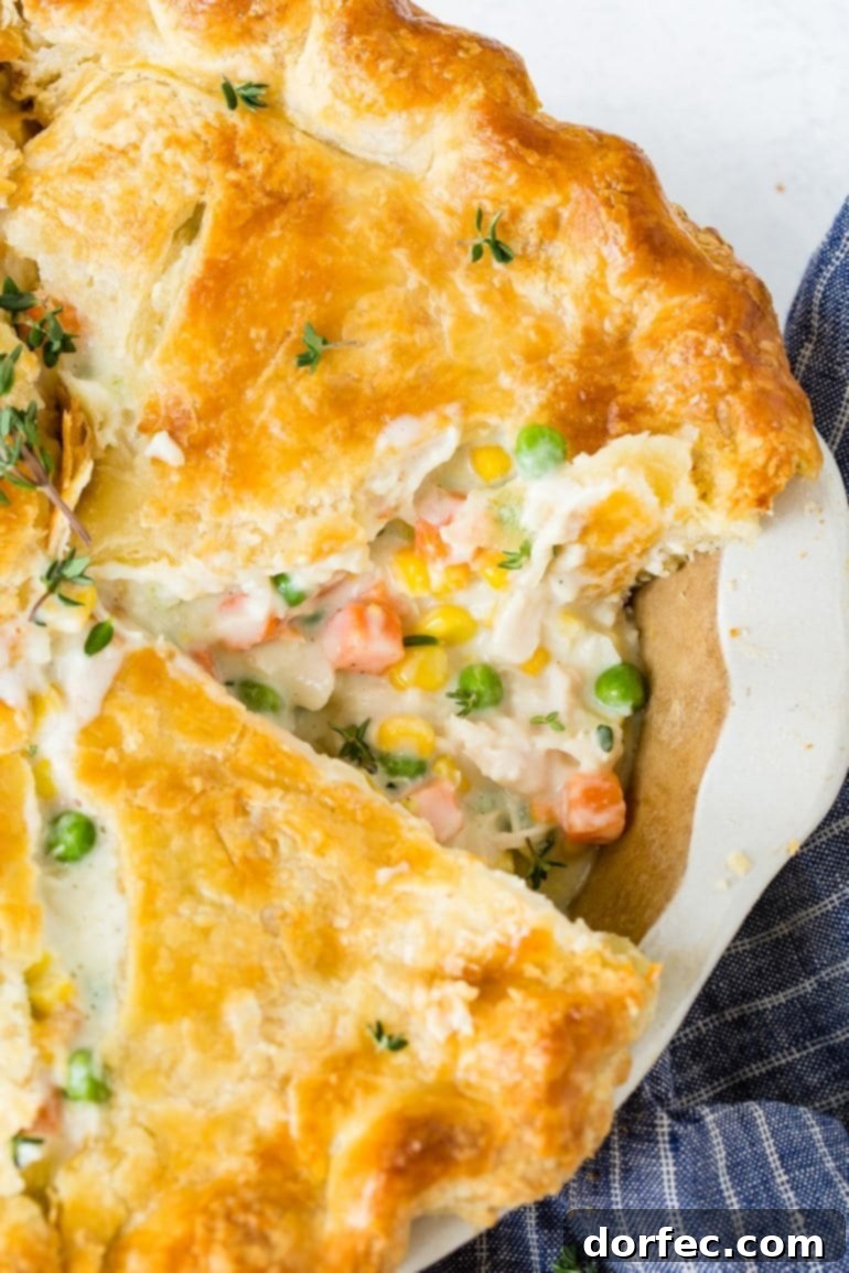 A whole, golden-brown homemade chicken pot pie with a single slice removed, revealing the rich, creamy filling packed with chicken, carrots, peas, and other vegetables.