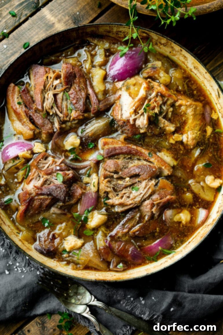 A hearty photo of tender chunks of braised pork butt nestled in a large Dutch oven, surrounded by a rich, glossy sauce, caramelized apple slices, sweet onion slices, and fragrant fresh herbs, ready to be served.