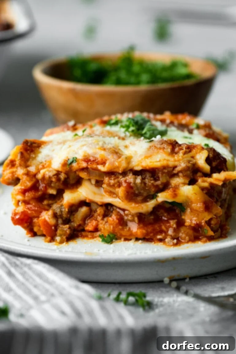 Weekly Menu Plan - Feb. 12-18 9 a photo of a serving of layered hearty meat lasagna on a white plate topped with melted cheese and chopped parsley