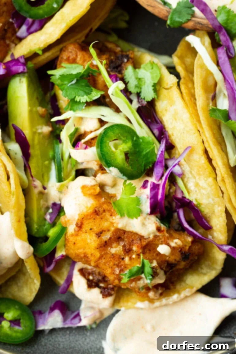 A stunning close-up of a perfectly constructed fish taco, featuring golden-brown, tender fish adorned with shredded cabbage, vibrant jalapeño slices, fresh chopped cilantro, and a generous dollop of creamy fish taco sauce. It's an irresistible symphony of flavors and textures.