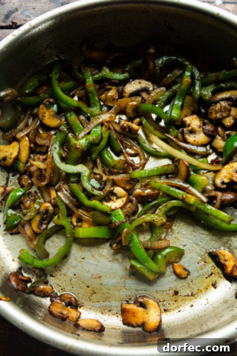A photo of sliced bell peppers and onions being expertly sautéed in a skillet alongside sliced mushrooms, creating a colorful and aromatic base for the creamy chicken.