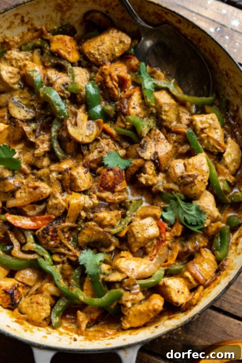 A vibrant photo of a skillet overflowing with golden cooked chicken chunks, sautéed bell peppers, onions, and mushrooms, all generously coated in a creamy sauce and beautifully garnished with chopped cilantro.