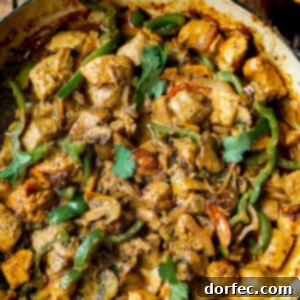 A photo of a skillet full of golden chicken chunks, sauteed bell pepper slices, onion slices, and sliced mushrooms in a creamy sauce, garnished with fresh cilantro.