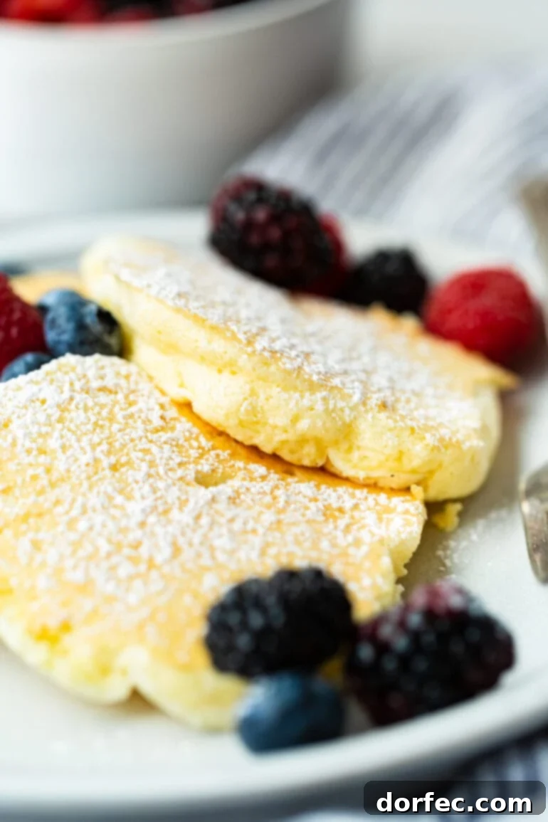 a photo of three fluffy golden Japanese cloud pancakes on a plate topped with powdered sugar and mixed fresh berries