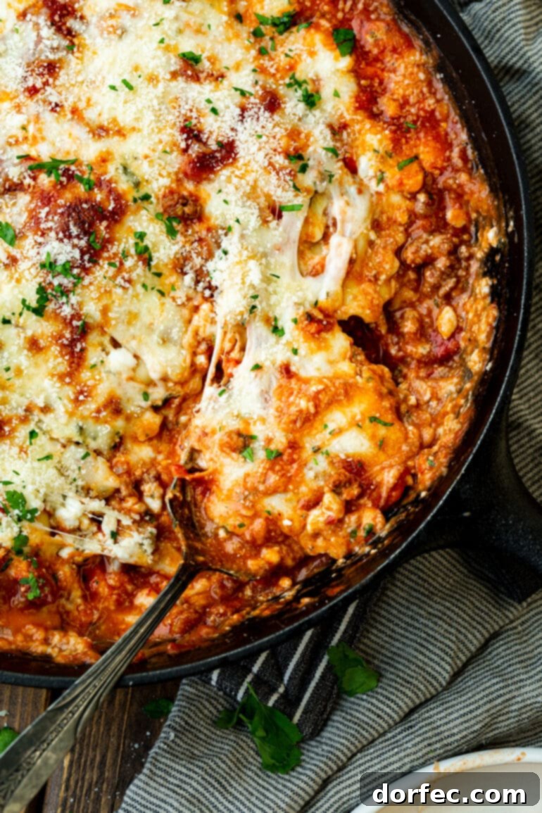 Effortless Skillet Ravioli Lasagna 2 A photo of a serving of skillet lasagna being scooped out of a cast iron skillet, showcasing its layers of pasta, meat sauce, and melted cheese.