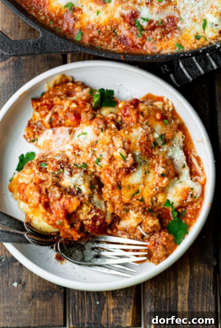 Effortless Skillet Ravioli Lasagna 3 A close-up photo of a serving of ravioli lasagna on a white dinner plate, with two forks poised to dig in.