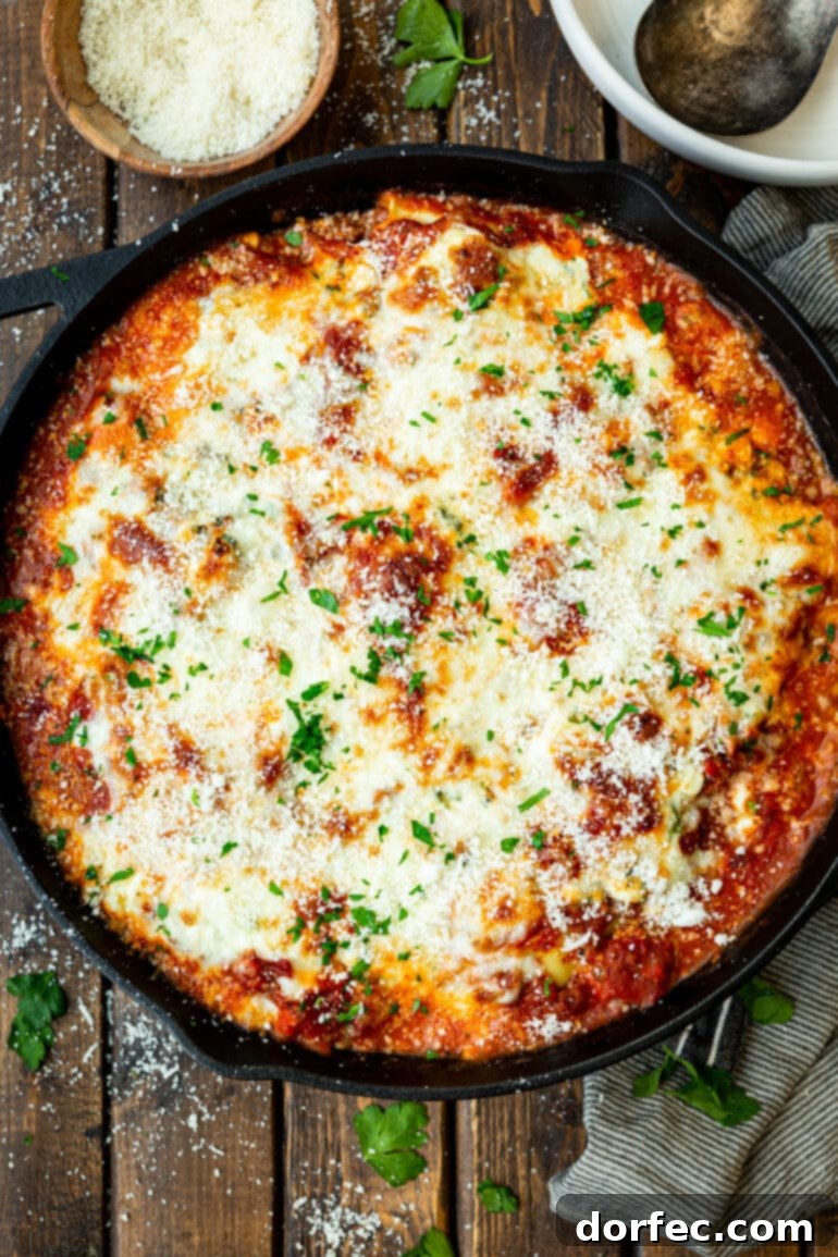 Effortless Skillet Ravioli Lasagna 5 A photo of a cast iron skillet full of lazy lasagna, topped with perfectly melted mozzarella cheese and freshly chopped parsley, ready to be served.