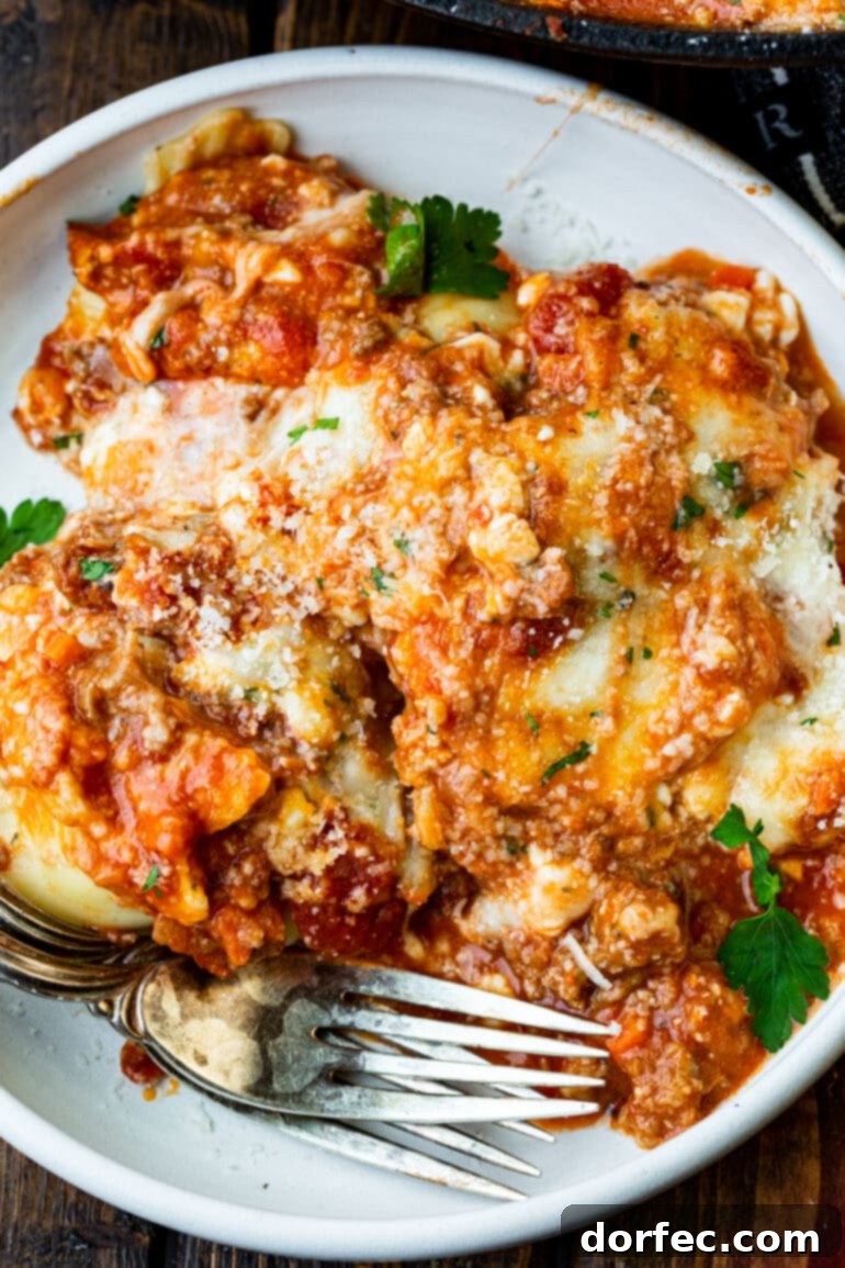 Effortless Skillet Ravioli Lasagna 6 A photo of a serving of lazy ravioli skillet lasagna on a white dinner plate, perfectly layered and topped with fresh herbs.