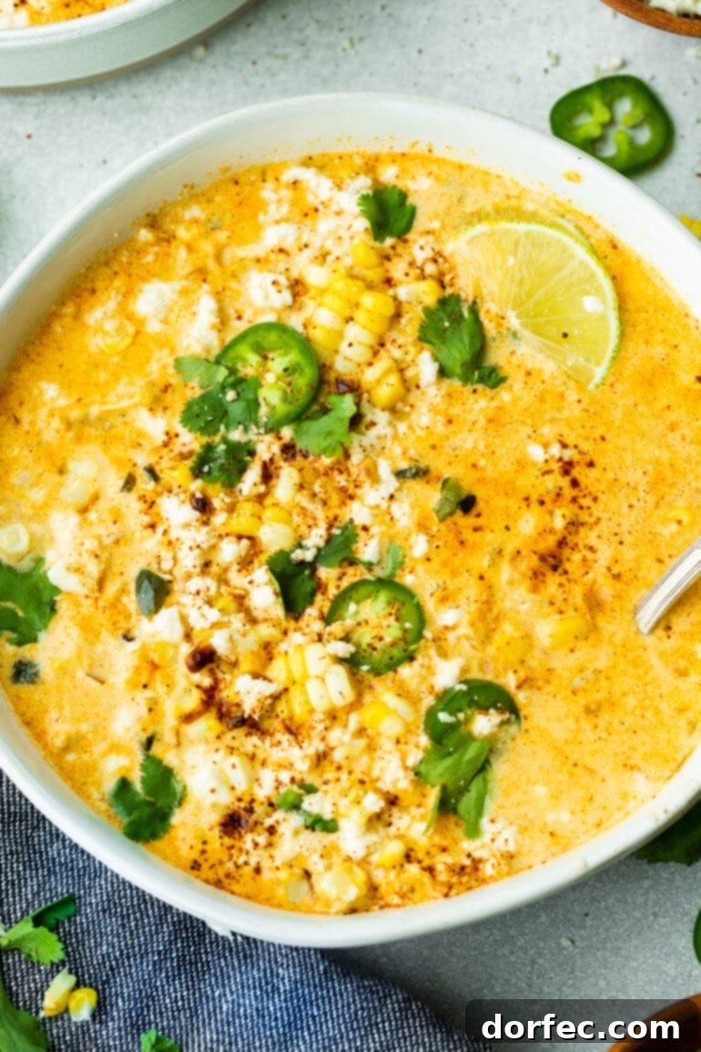 A large, inviting bowl of creamy Mexican Street Corn Soup (Elote Soup), generously topped with fresh cilantro, vibrant lime wedges, crumbled cotija cheese, and spicy jalapeño slices.