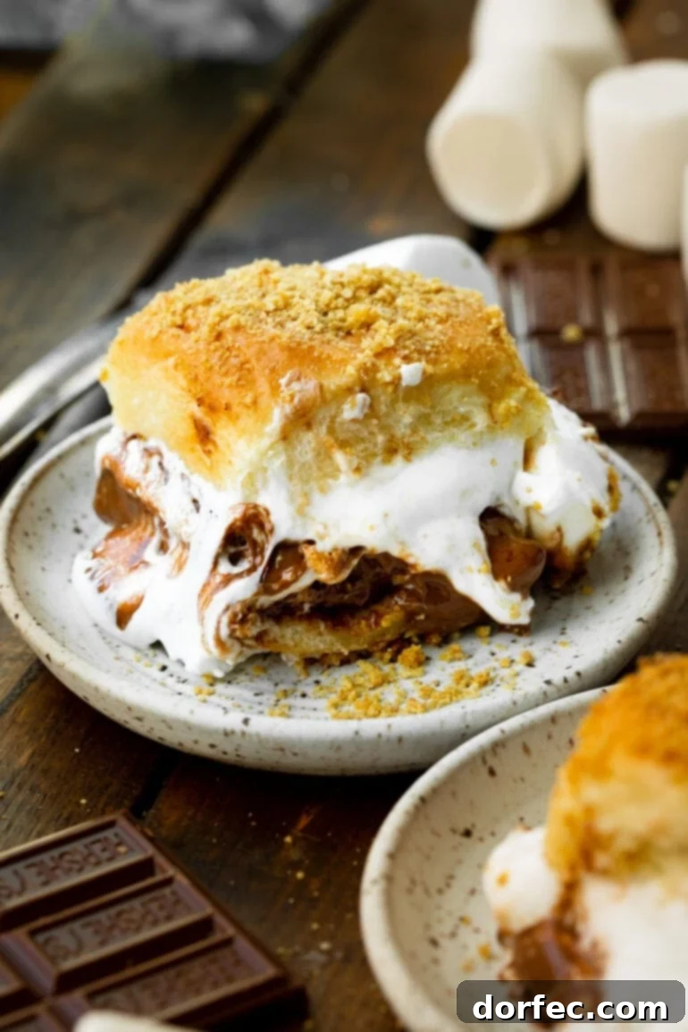 S'mores Sliders 2 A delicious s'mores slider on a small dessert plate, with gooey melted marshmallows and rich chocolate oozing out from sweet Hawaiian rolls.