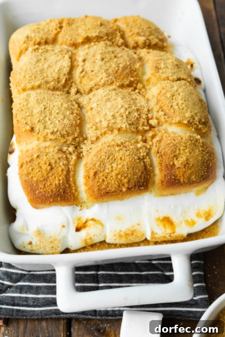 S'mores Sliders 3 A casserole dish filled with a dozen golden-brown s'mores sliders, showcasing melted marshmallow and chocolate oozing from the sides, topped with a sprinkle of graham cracker crumbs.
