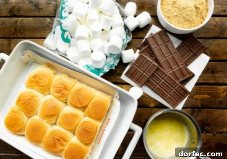 S'mores Sliders 4 A flat lay photo displaying all the essential ingredients for s'mores sliders: Hawaiian sweet rolls, a bowl of melted butter, a bag of large marshmallows, Hershey's chocolate bars, and a bowl of graham cracker crumbs.