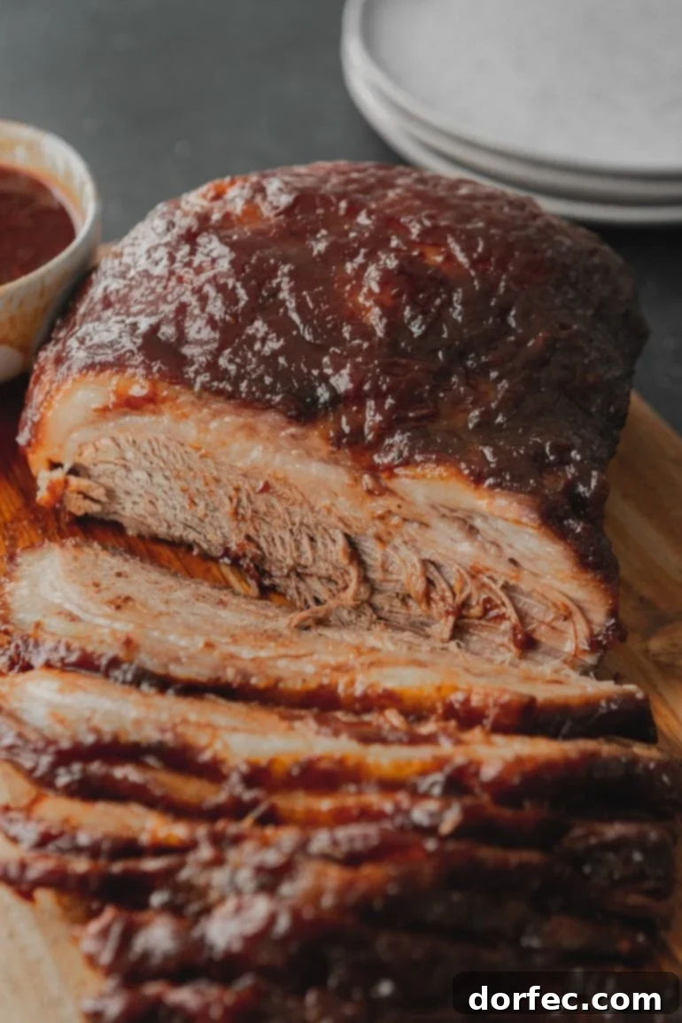 A partially sliced, incredibly tender beef brisket, glazed with a rich BBQ sauce and ready to be served, showcasing its delicious, fall-apart texture.