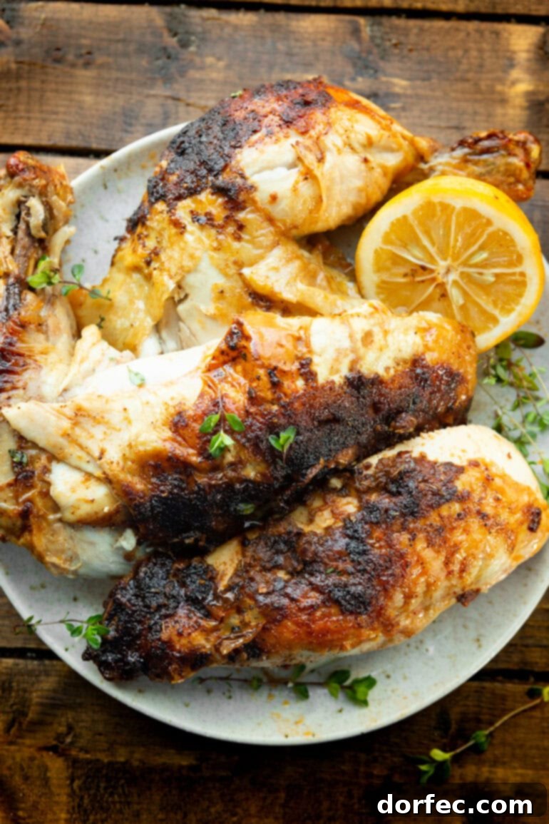 A photo of a deconstructed whole air-fried chicken, showcasing its crispy golden skin and tender meat, with half a lemon for garnish.