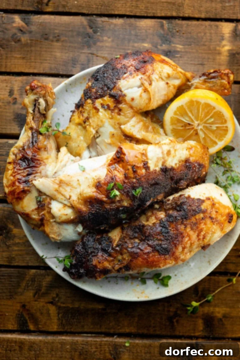 A photo of a perfectly air-fried whole chicken, expertly broken down into individual serving pieces, presented alongside a half lemon.