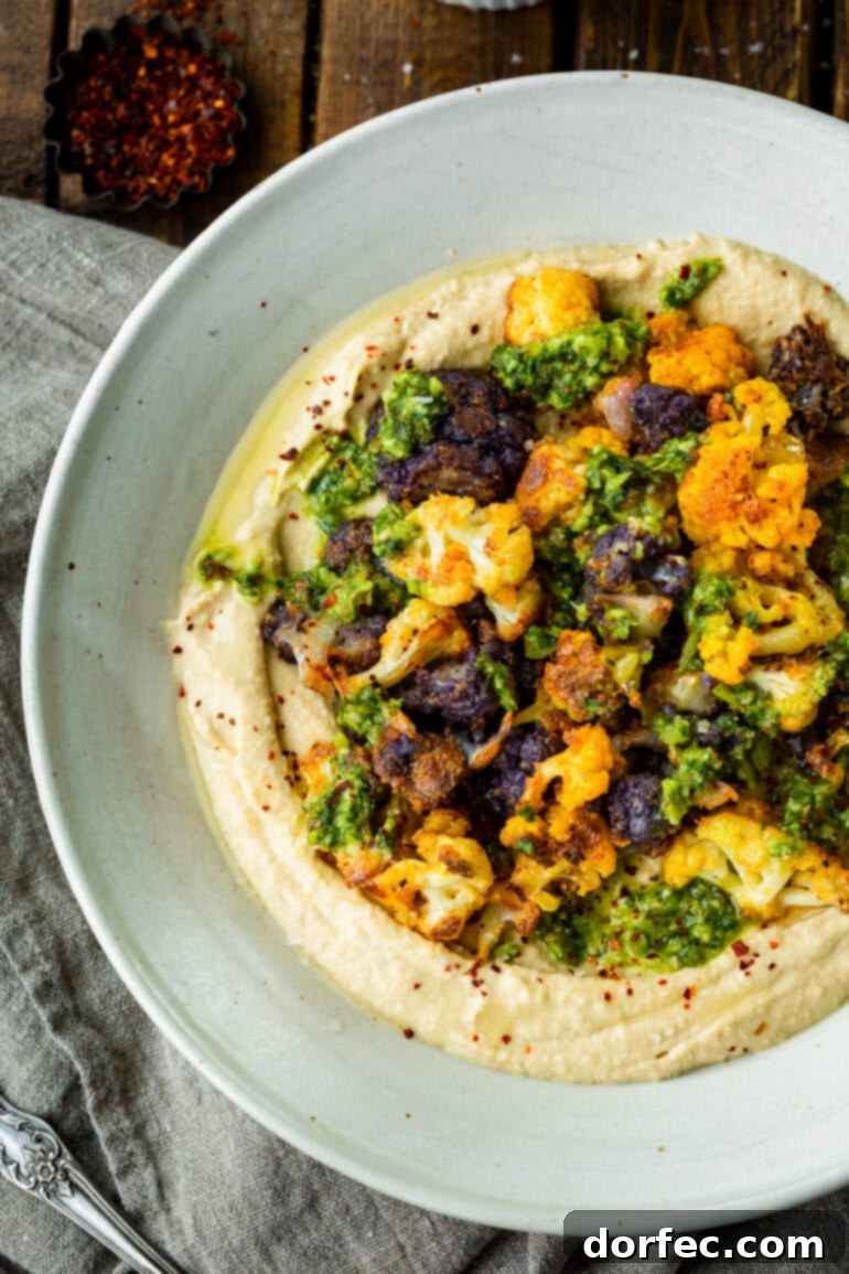 A photo of beautifully roasted white and purple cauliflower florets, golden and crisp, served on a creamy bed of hummus and topped with vibrant green pesto sauce, ready to be enjoyed as a healthy and flavorful meal.