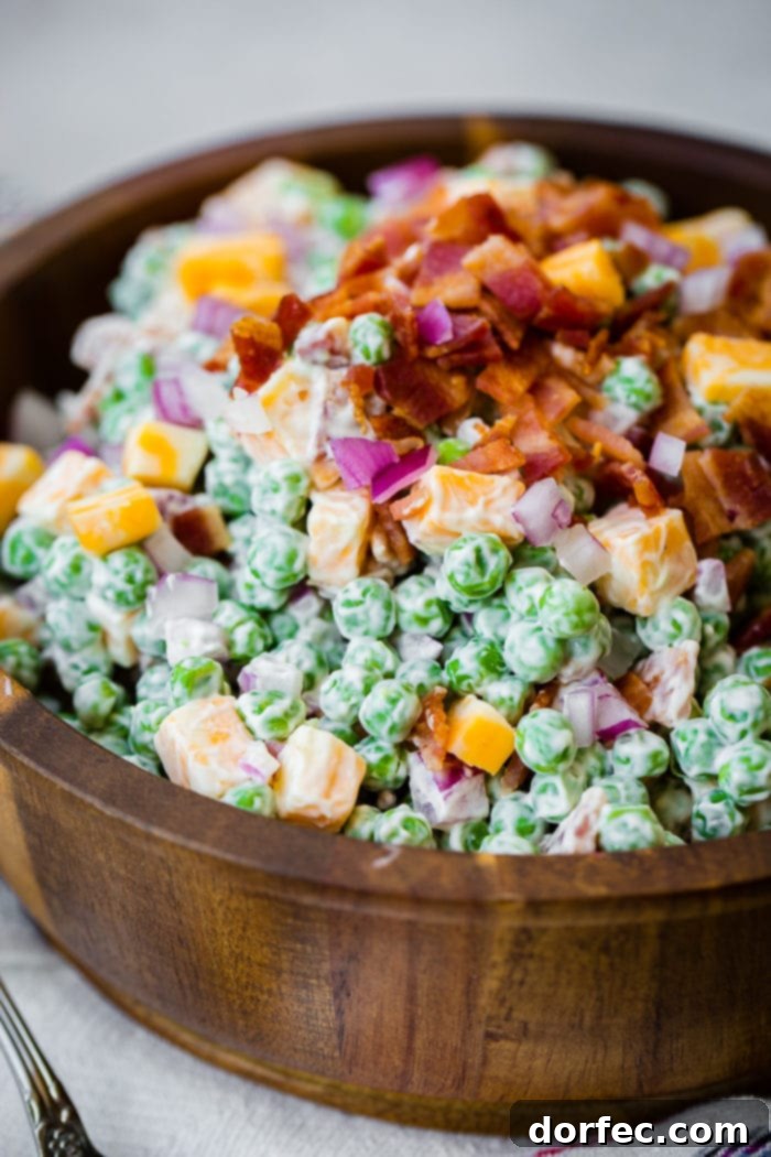 a wooden bowl full of creamy southern english pea salad with bacon, chunks of colby jack cheese
