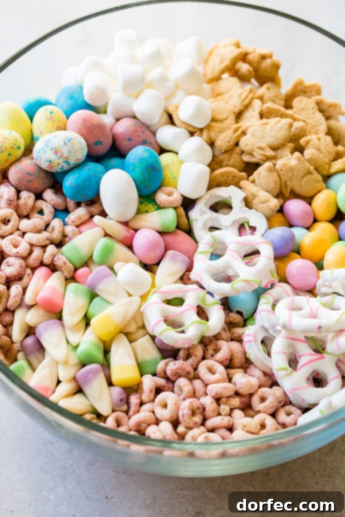 Easter snack mix in a clear glass bowl with berry Cheerios, Easter candy corns, yogurt covered pretzels, Robin eggs, Easter M&Ms. mini marshmallows and bunny cookies.