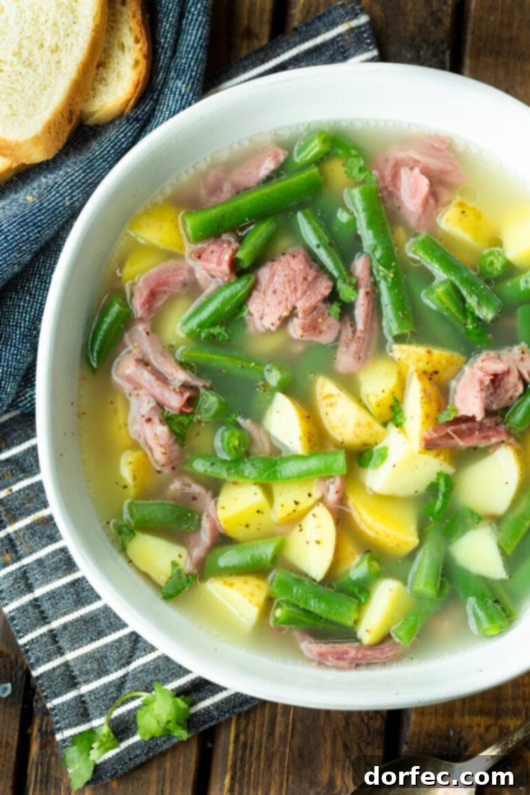 A rustic bowl of hearty ham hock soup, brimming with tender potatoes, green beans, and generous pieces of ham.