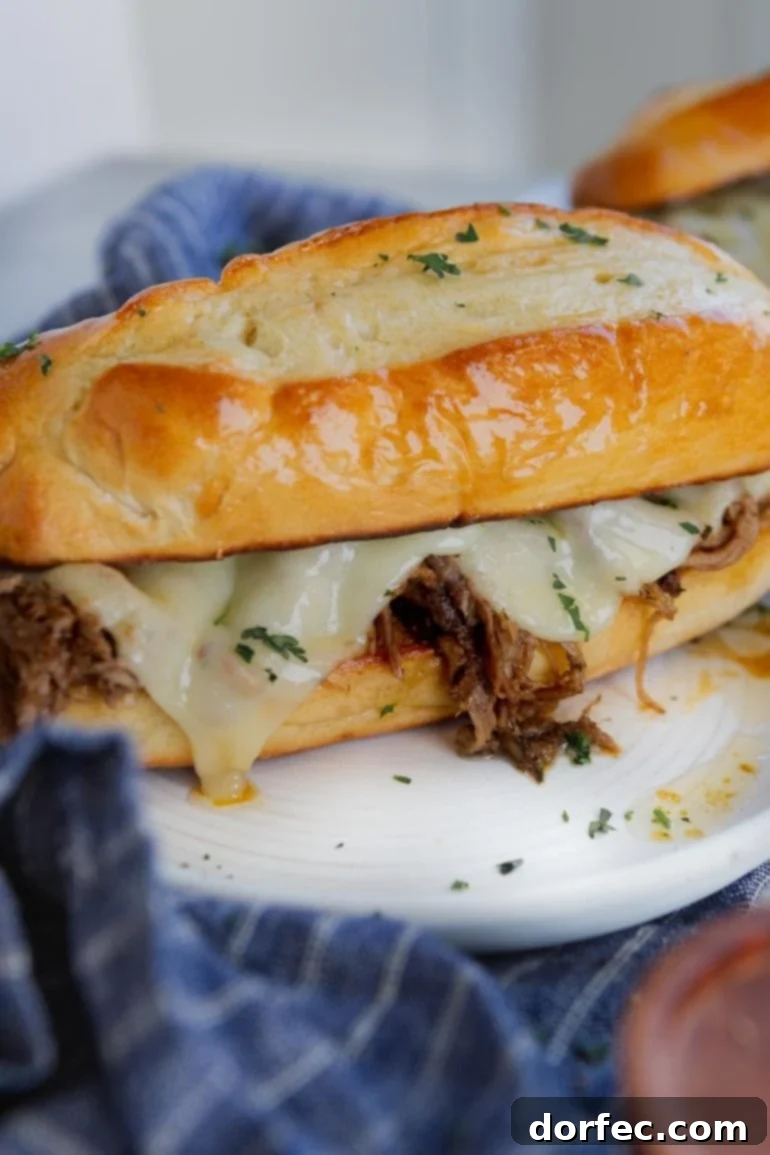 Your Weekly Meals April 8-14 3 A delectable French dip sandwich featuring tender beef and melted cheese on a golden hoagie roll, served on a plate with a blue and white napkin underneath, ready for dipping into savory au jus.
