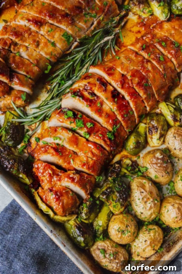 Two beautifully glazed and roasted pork loins, elegantly sliced for serving, presented on a sheet pan alongside perfectly roasted potatoes and vibrant Brussels sprouts, making for a complete and impressive meal.