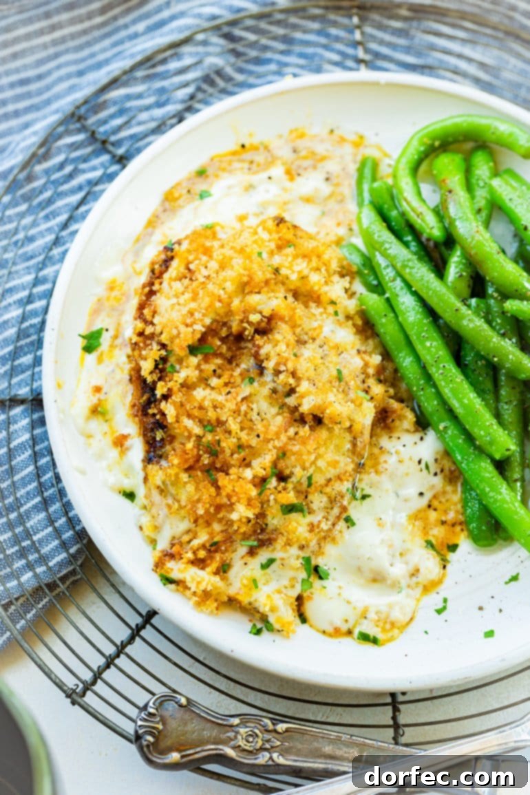 a photo of a single panko covered chicken breast sitting in a creamy sauce with a serving of fresh green beans on the side.