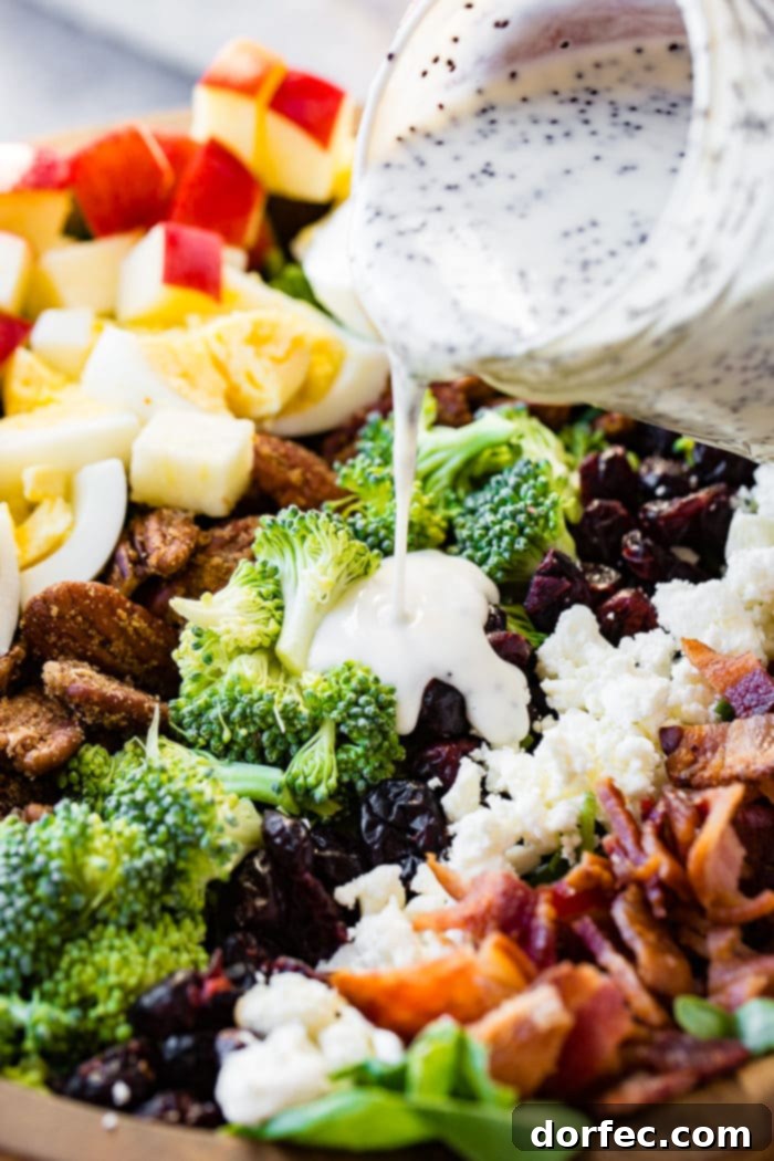 a wooden bowl full of a harvest cobb salad with maple poppy seed dressing. Hardboiled eggs, brown sugar pecans, broccoli, craisins, apples, feta and kale
