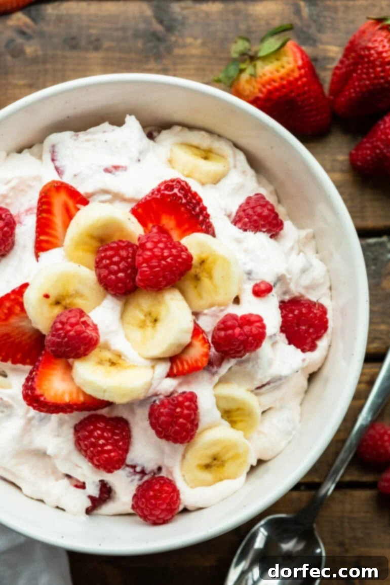 Dreamy Fluffy Cheesecake Fruit Salad 2 A beautifully presented bowl of creamy cheesecake fruit salad, garnished with fresh banana slices, whole raspberries, and sliced strawberries, ready to be served.