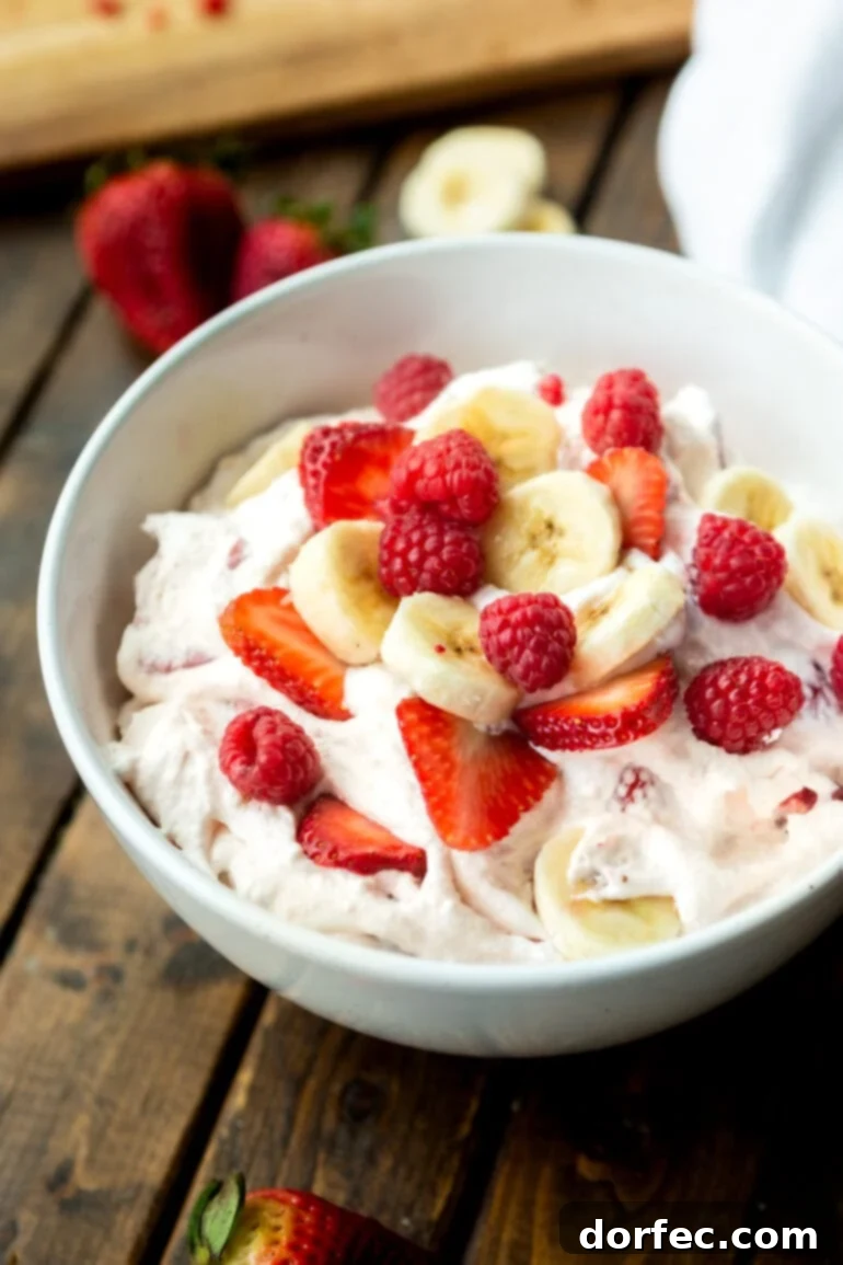 Dreamy Fluffy Cheesecake Fruit Salad 7 A large bowl filled with a colorful medley of sliced bananas, strawberries, and whole raspberries, all mixed generously with the creamy cheesecake pudding and yogurt base, ready to be chilled.