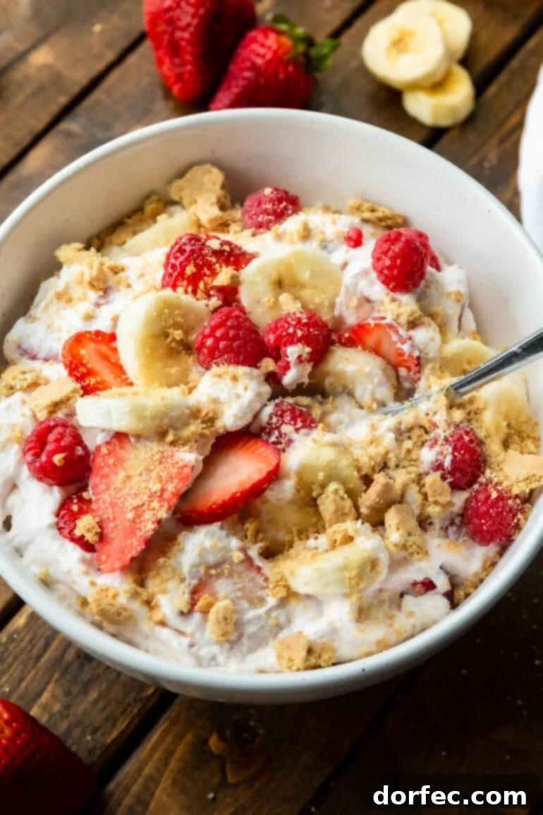 Dreamy Fluffy Cheesecake Fruit Salad 8 A bowl of creamy cheesecake fruit salad generously topped with crumbled graham crackers, showcasing sliced strawberries and bananas, ready to be enjoyed as a decadent side or dessert.