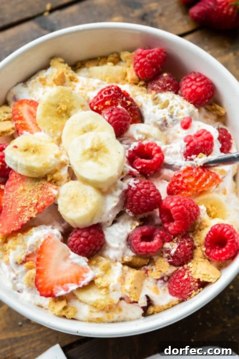 Dreamy Fluffy Cheesecake Fruit Salad 9 A vibrant and creamy fruit salad, featuring sliced bananas, strawberries, and raspberries, beautifully topped with a sprinkle of crushed graham crackers for an added cheesecake crunch.