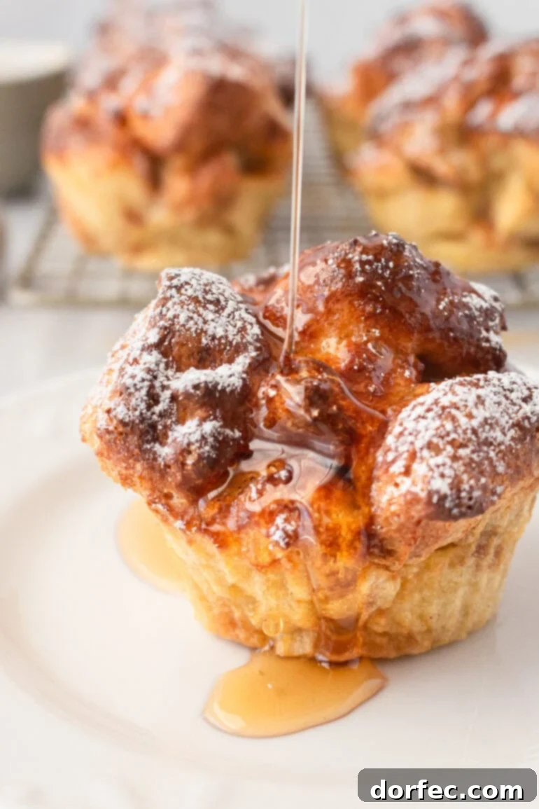 A golden French toast muffin, freshly baked, with powdered sugar delicately dusted over its surface, as warm maple syrup is drizzled down the side.