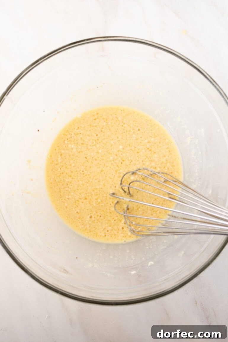 A bowl filled with whisked eggs, melted butter, and milk, forming the rich custard base.