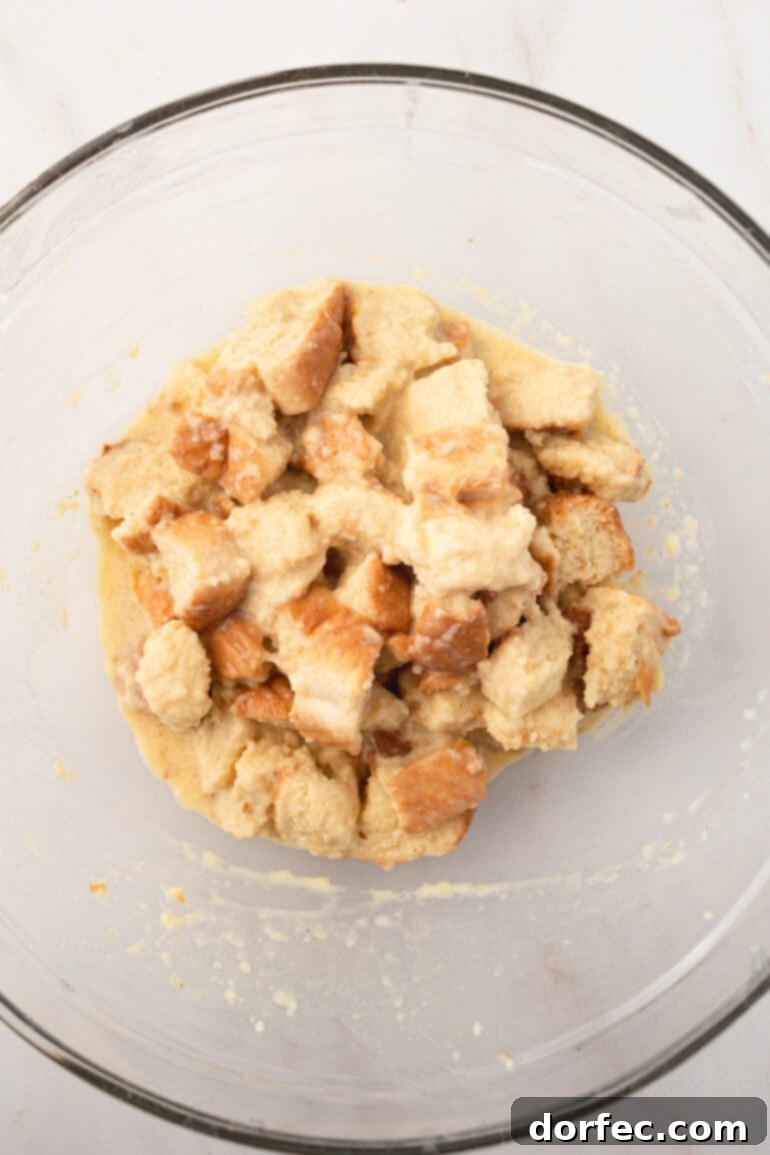 The bread cubes being tossed in the French toast custard, ensuring an even and thorough coating.