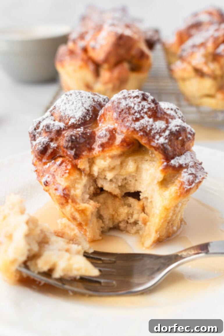A close-up shot of a golden-baked French toast muffin with a bite taken out, revealing its soft, fluffy, and custardy interior.