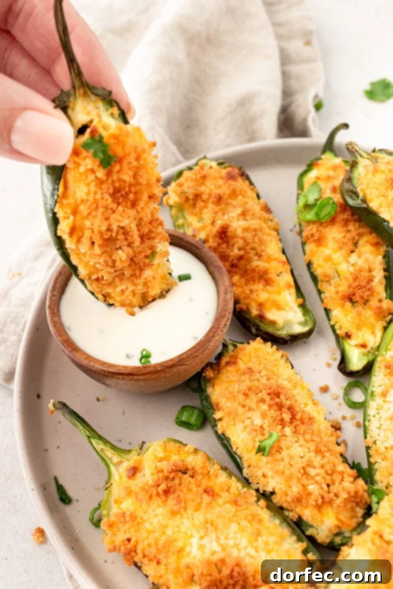 A hand dipping a golden crispy jalapeño popper into a small cup of ranch dressing, highlighting the perfect snack texture.