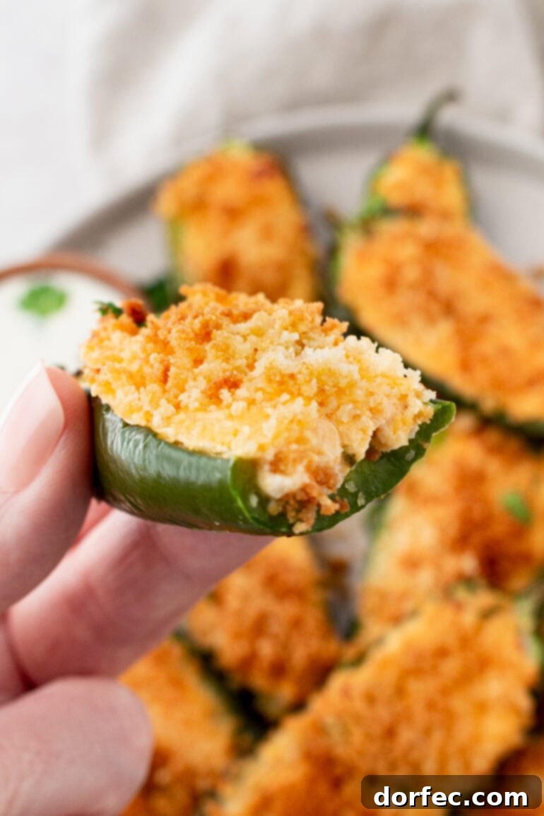 A hand holding a golden crispy air fryer jalapeño popper that has been bitten into, revealing the creamy cheese filling.