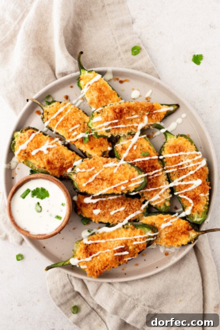 A plate full of crispy golden air fryer jalapeño poppers, lightly drizzled with a creamy garlic sauce.