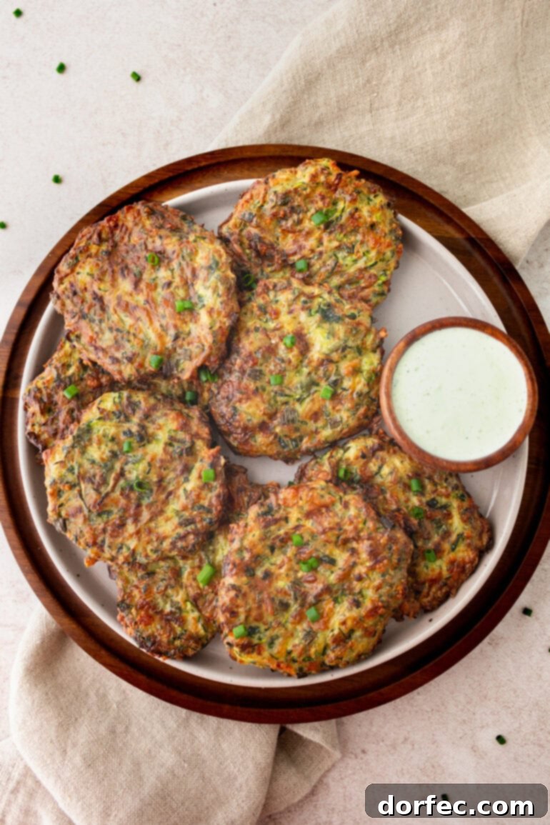 Crispy Parmesan Basil Zucchini Fritters 14 A close-up shot of several crispy golden zucchini fritters arranged on a plate next to a small dish of creamy dipping sauce, highlighting their appetizing appeal.