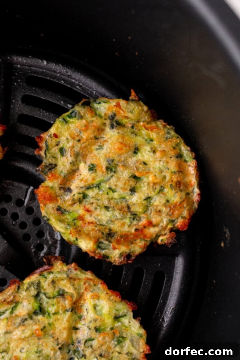 Crispy Parmesan Basil Zucchini Fritters 8 A delicious batch of Parmesan Basil Zucchini Fritters sizzling in an air fryer basket, achieving a perfect golden-brown crispness with minimal oil.