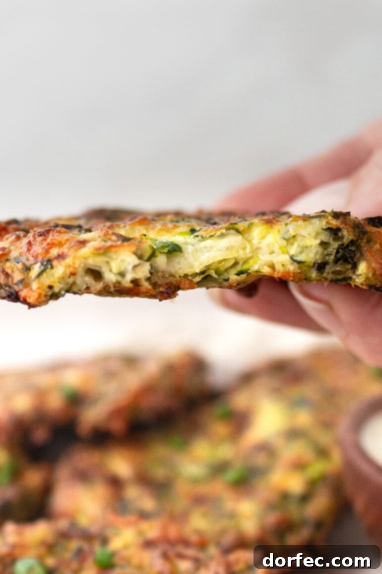 Crispy Parmesan Basil Zucchini Fritters 10 A close-up of someone holding a single, perfectly cooked zucchini fritter with a bite taken out, revealing the soft, cheesy interior and crisp exterior.