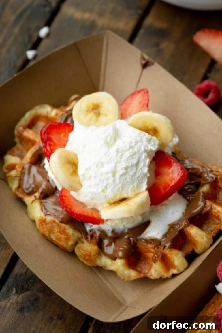 A photo of a large Liege waffle topped with melting Nutella, sliced strawberries and bananas, and a dollop of crème fraîche. Topping ideas for homemade Liege waffles.