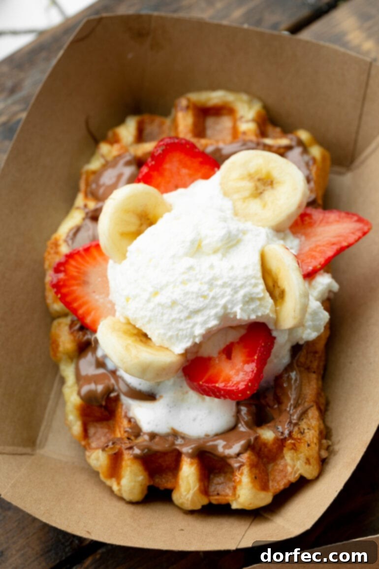 A photo taken over the top of a golden Liege waffle topped with Biscoff cookie butter, sliced strawberries and bananas, and whipped cream. Family favorite waffle toppings.