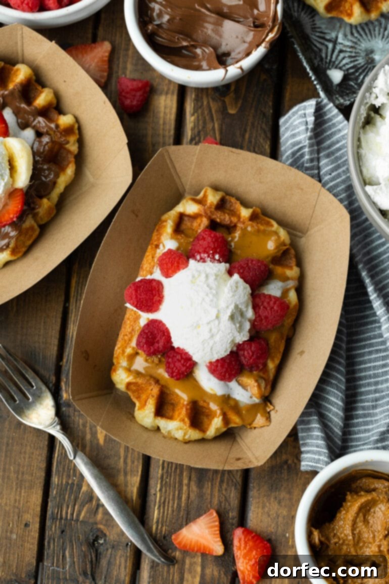 A photo of a Liege waffle in a brown cardboard container topped with Biscoff cookie butter, fresh raspberries, and a scoop of whipped cream. A delicious breakfast or dessert.