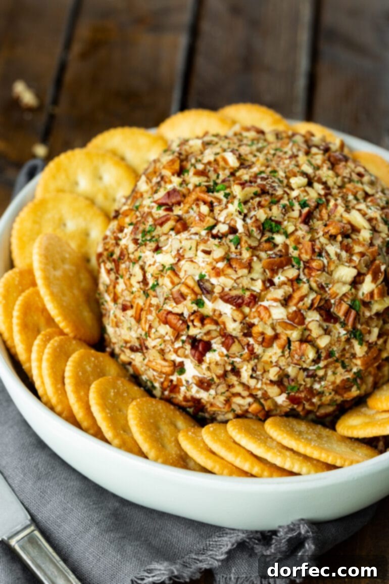 A large, beautifully crafted cheese ball, generously coated in chopped pecans and fresh parsley, surrounded by Ritz crackers.