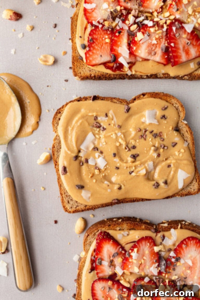 Several slices of multigrain toast are artfully arranged, some topped with creamy coconut peanut butter, while others are garnished with vibrant sliced strawberries.
